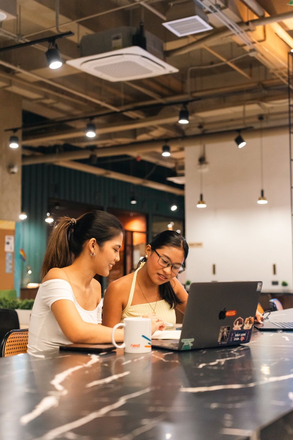 Two women studying together with laptops at a marble table